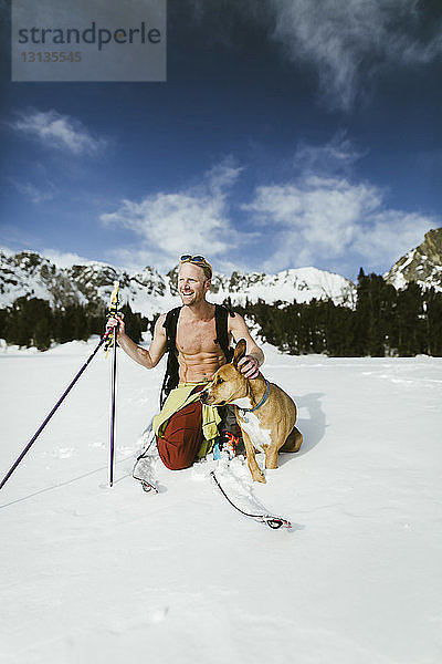 Fröhlicher Wanderer mit Hund auf verschneitem Feld gegen Berge