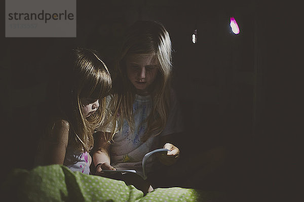 Mädchen lesen zu Hause in dunklem Raum Buch