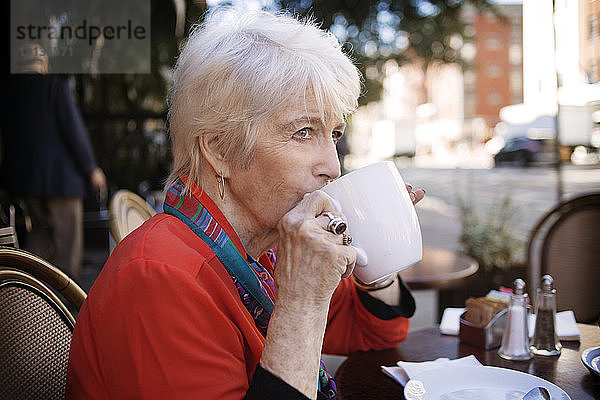 Ältere Frau trinkt Kaffee im Straßencafé