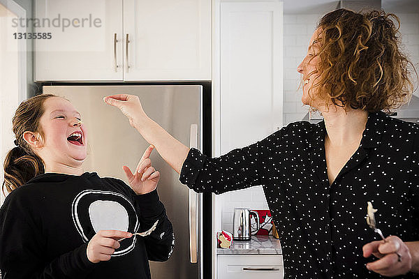 Verspielte Mutter mit Tochter steht am Kühlschrank in Küche und Haushalt