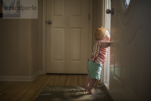 Seitenansicht eines kleinen Jungen  der durch die Tür schaut