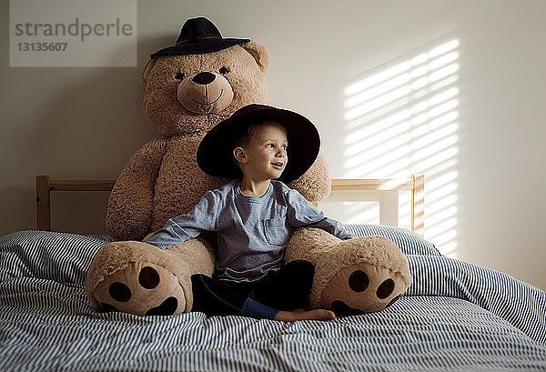 Junge mit Teddybär sitzt zu Hause auf dem Bett