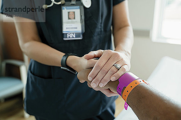 Nahaufnahme einer Krankenschwester  die auf der Krankenhausstation die Hand eines älteren Patienten hält