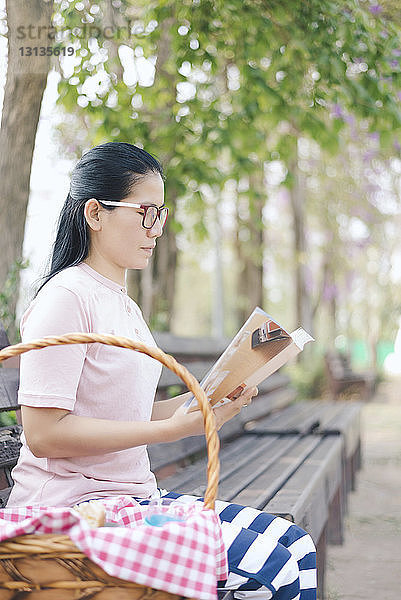 Frau liest Buch  während sie im Park auf einer Bank sitzt