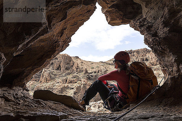 Fröhliche Rucksacktouristin sitzt am Eingang einer Höhle in einer Felsformation