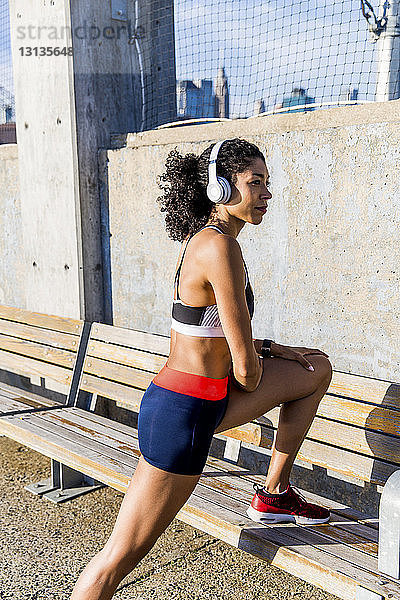 Sportlerin hört Musik  während sie an einem sonnigen Tag auf einer Bank trainiert