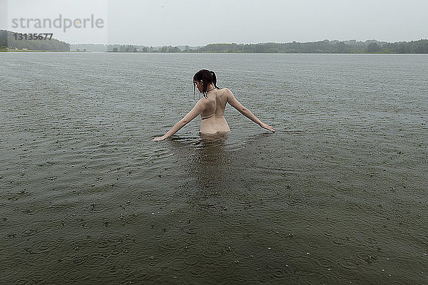 Rückansicht einer jungen Frau ohne Hemd  die während der Regenfälle im See steht