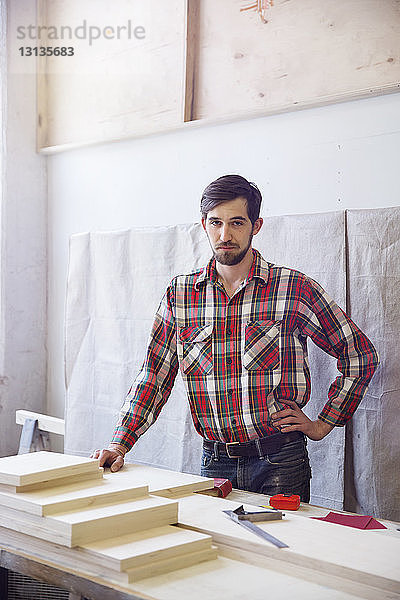 Selbstbewusster Handwerker steht an der Werkbank in der Holzwerkstatt