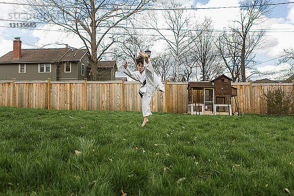 Junge in Sportuniform tritt in die Luft  während er im Hinterhof Karate übt