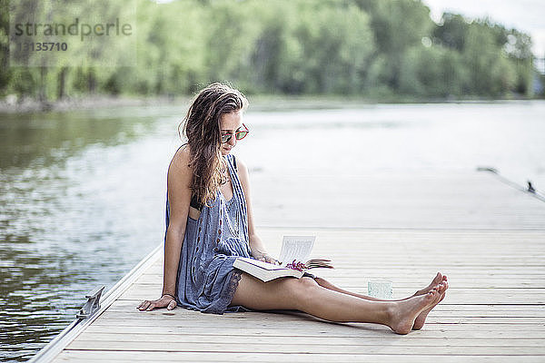 Frau liest Buch  während sie sich am Pier über dem See ausruht