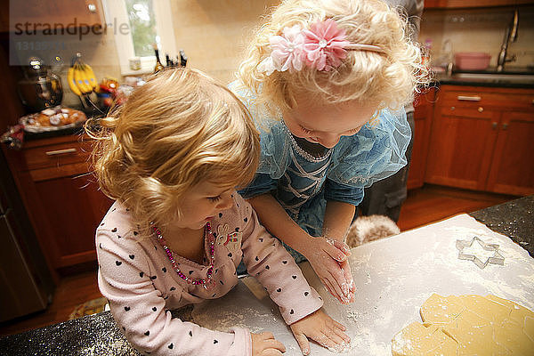 Schrägaufnahme von glücklichen Schwestern  die zu Hause in der Küche Kekse backen