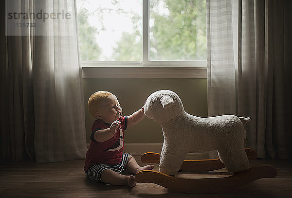 Kleiner Junge spielt mit Lammwippe  während er zu Hause auf dem Boden sitzt