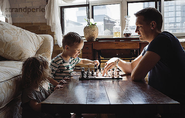 Seitenansicht eines Vaters  der zu Hause mit Kindern auf dem Tisch Schach spielt