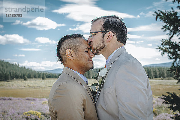 Mann küsst seinen Freund auf die Stirn  während er vor bewölktem Himmel steht