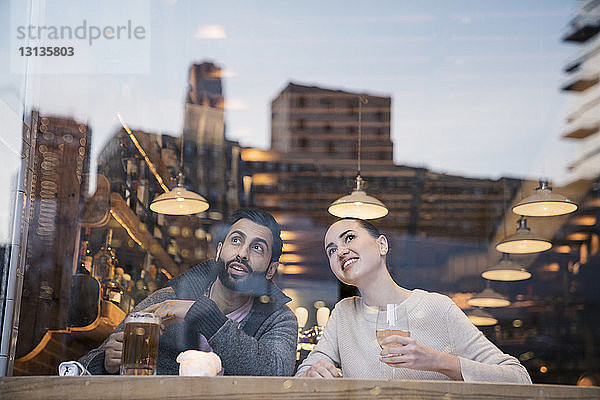 Ein Paar genießt Getränke  während es durch ein Restaurantfenster wegschaut