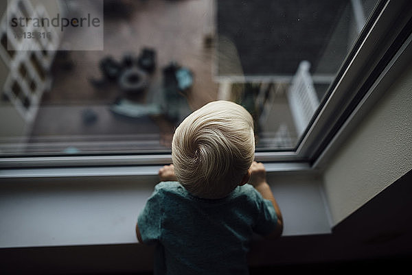 Rückansicht eines zu Hause stehenden kleinen Jungen  der durch ein Fenster schaut