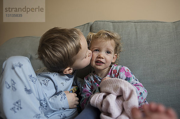Junge küsst Schwester  während er zu Hause auf dem Sofa sitzt