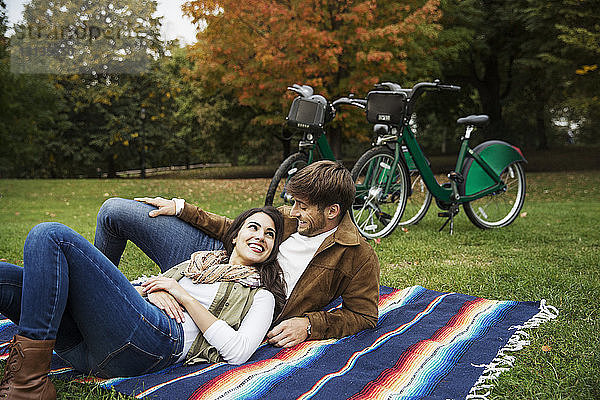 Glückliches Paar sieht sich an  während es sich auf einer Decke im Park entspannt