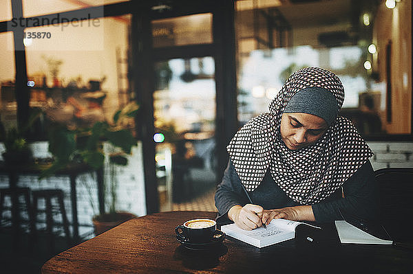 Frau schreibt in Buch im Café