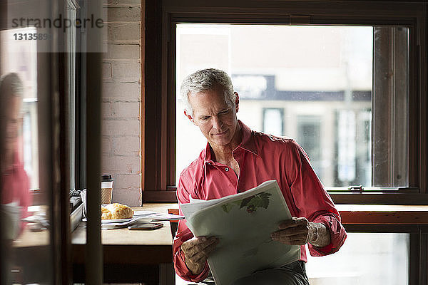 Reifer Mann liest Zeitung bei Kaffee und Croissant im Café