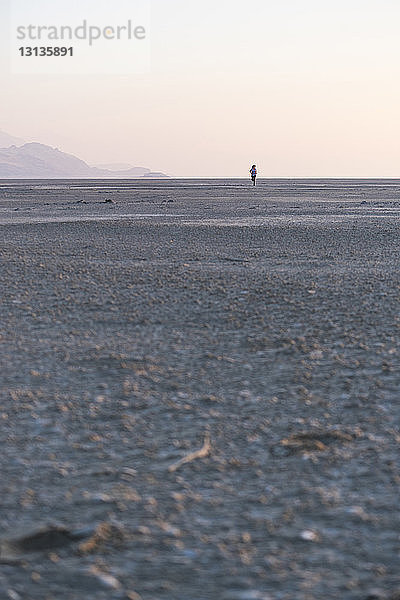 Fernblick einer Frau  die am Strand gegen den klaren Himmel bei Sonnenuntergang auf Sand läuft