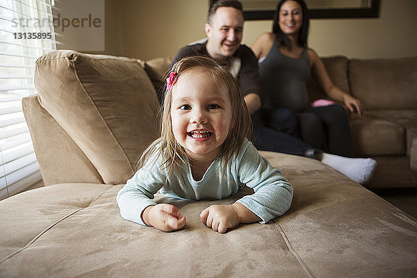 Porträt eines niedlichen Mädchens  das liegt  während die Eltern zu Hause auf dem Sofa sitzen