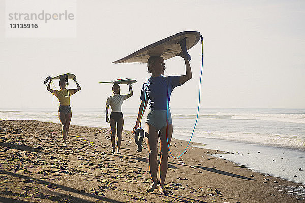 Freunde tragen Surfbrett beim Strandspaziergang gegen den Himmel