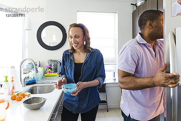 Glückliche Frau hält Schüssel  während der Mann in der Küche den Kühlschrank öffnet