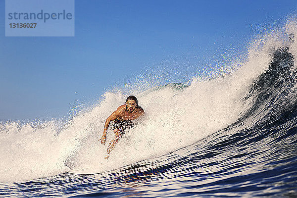 Mittelgroßer erwachsener Mann surft im Meer vor klarem blauen Himmel
