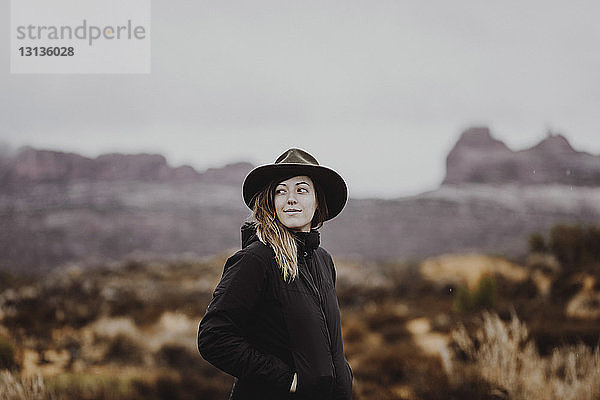 Frau mit Hut schaut weg  während sie in der Wüste gegen den Himmel steht