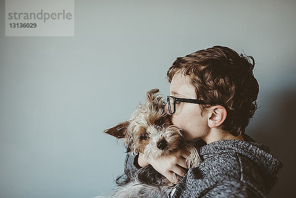 Seitenansicht eines Jungen  der zu Hause Yorkshire Terrier gegen die Wand küsst