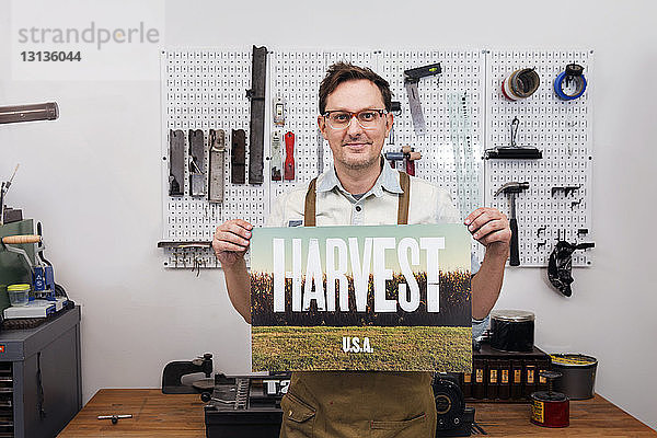 Männlicher Handwerker hält Poster und steht in der Werkstatt