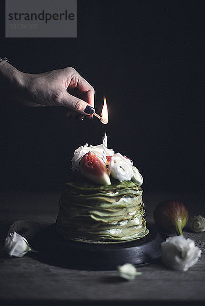 Beschnittenes Bild einer Frau  die eine Blitzkerze auf einem Pfannkuchen anzündet