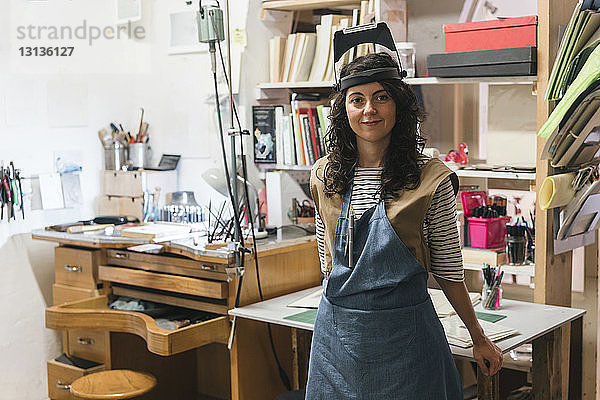 Porträt einer selbstbewussten Kunsthandwerkerin  die im Workshop am Tisch steht