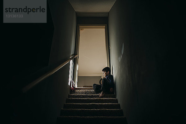 Niedrigwinkelansicht eines Jungen  der auf Stufen an der Haustür sitzt