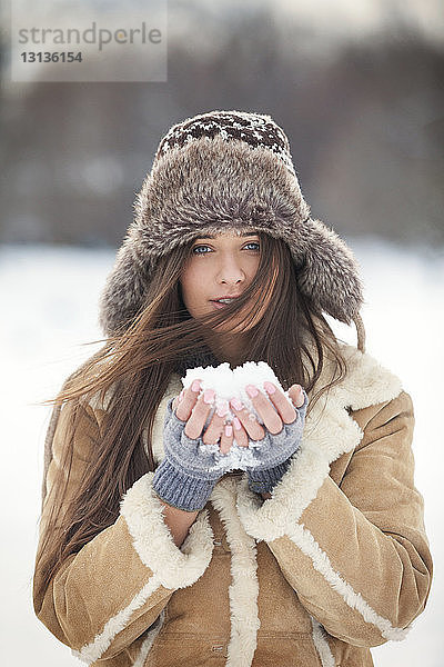 Porträt einer schönen Frau in warmer Kleidung  die Schnee hält
