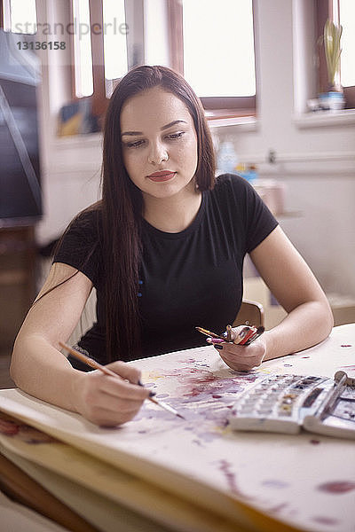 Frau malt auf Papier  während sie zu Hause sitzt