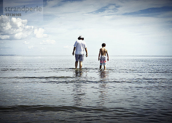 Rückansicht von Vater und Sohn beim Spaziergang im Meer gegen den Himmel