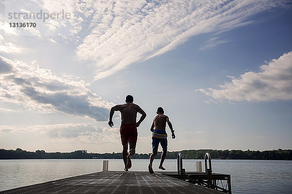 Rückansicht von Vater und Sohn beim Laufen auf dem Pier am See