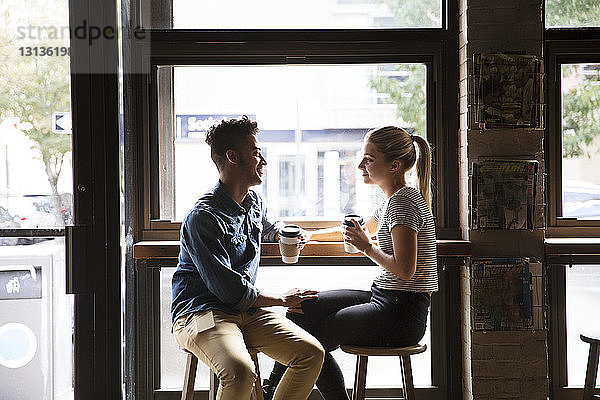 Lächelndes Paar unterhält sich  während es im Café am Fenster sitzt