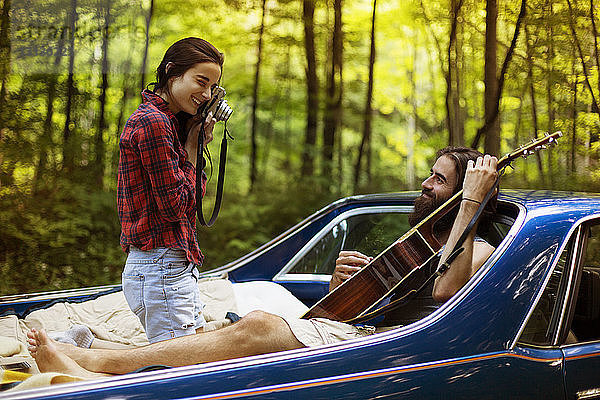 Frau fotografiert Freund mit Gitarre im Pick-up im Wald