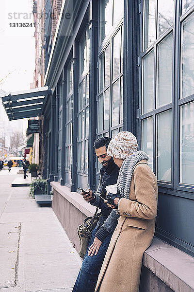 Paar benutzt Mobiltelefon beim Anlehnen am Gebäude in der Stadt