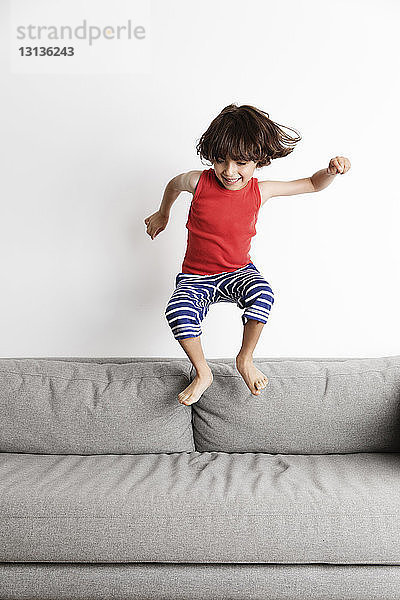 Glücklicher Junge springt zu Hause auf dem Sofa gegen die Wand