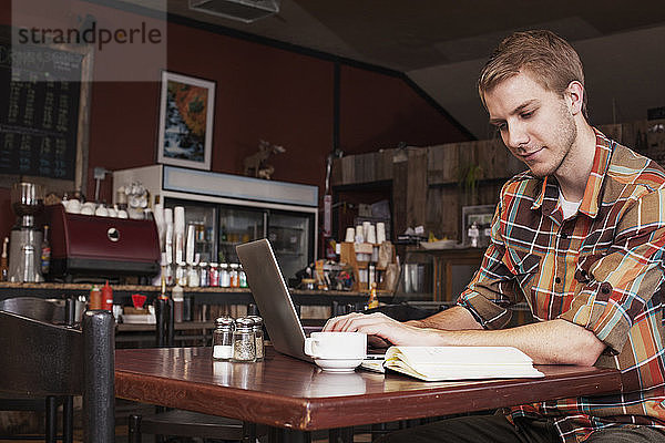 Mann arbeitet am Laptop  während er im Café sitzt
