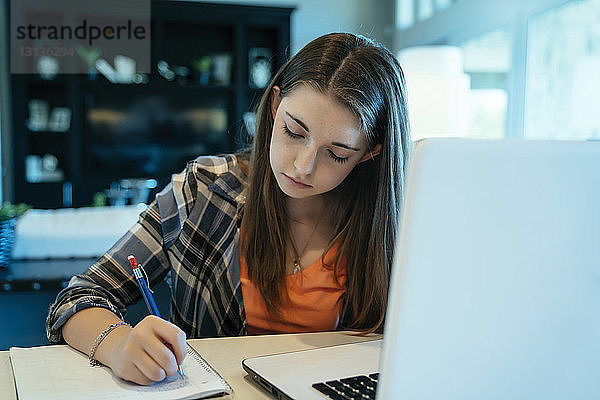 Teenagerin macht Hausaufgaben mit Laptop zu Hause