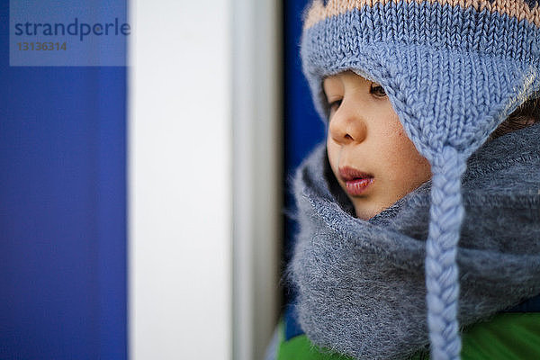 Nahaufnahme eines nachdenklichen Jungen in warmer Kleidung  der weg schaut  während er an der Tür steht