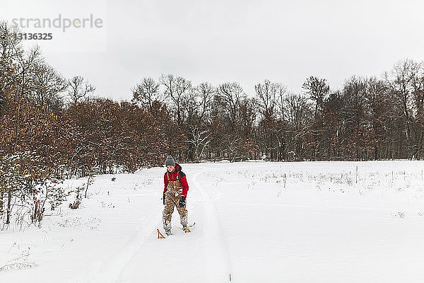Teenager Junge mit Schneeschuhen auf schneebedecktem Feld im Wald gegen den Himmel