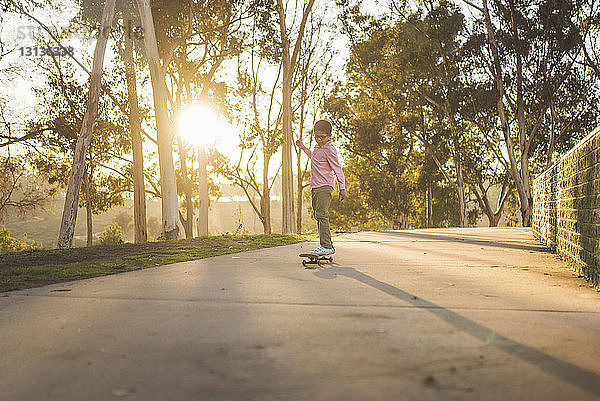 Seitenansicht eines Jungen  der bei Sonnenuntergang auf einem Fußweg im Park Skateboard fährt
