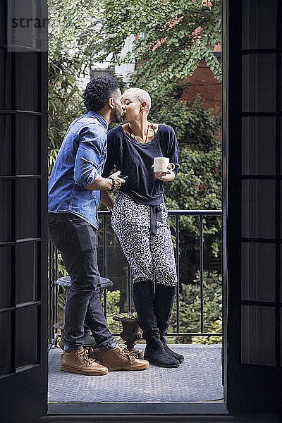 Romantisches Paar küsst sich  während es auf dem Balkon steht und durch die Tür gesehen wird