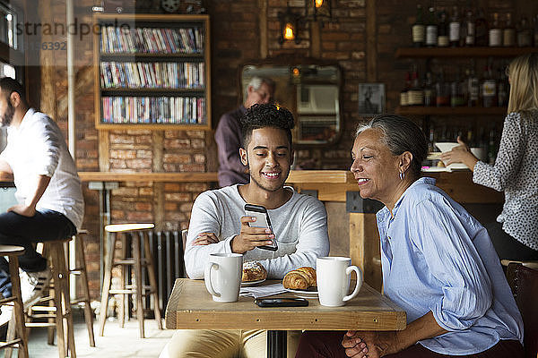 Lächelnder Mann zeigt Frau Telefon  während sich Kunden im Café entspannen